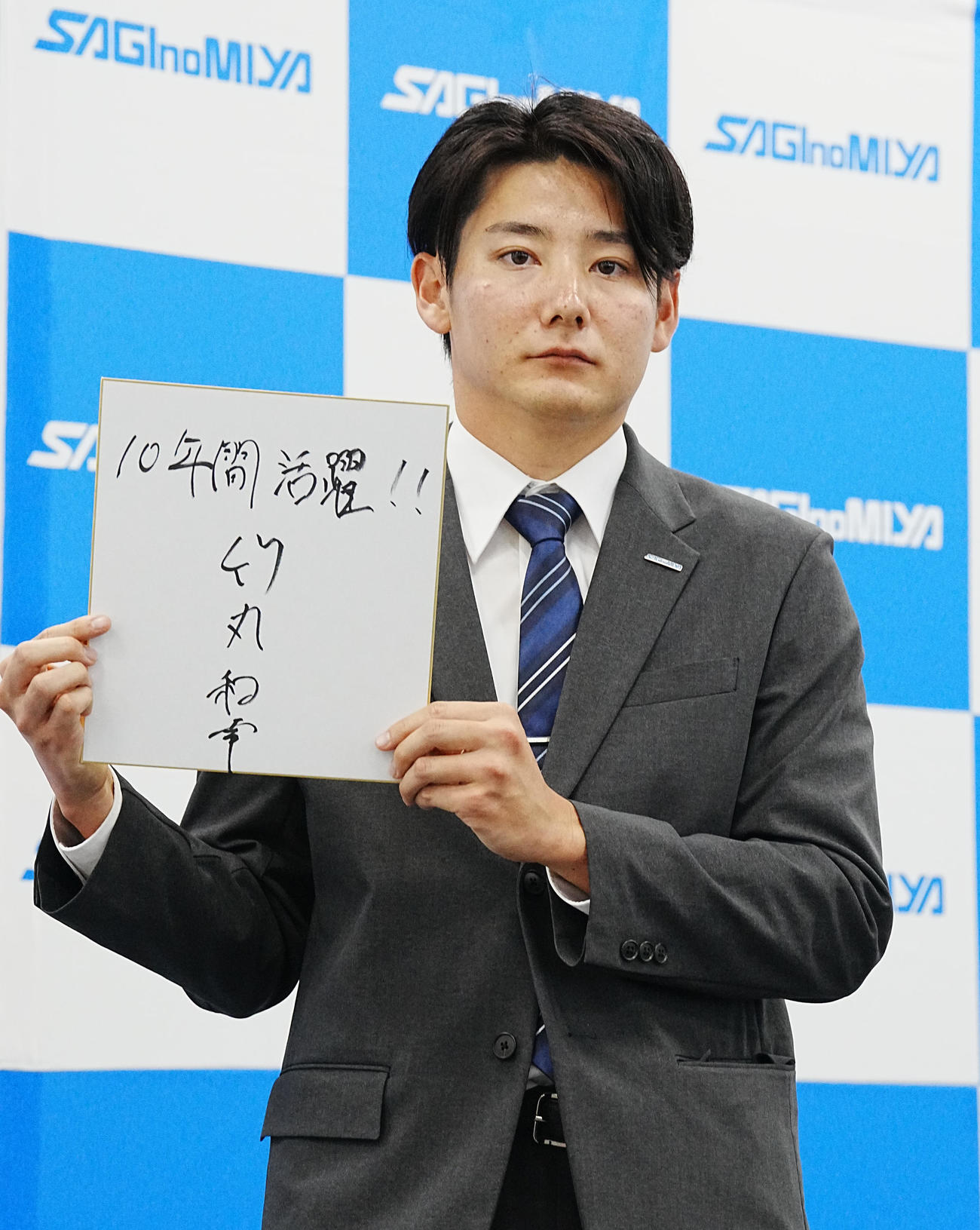 巨人からドラフト1位指名を受けた鷺宮製作所・竹丸はトレードマークのポーカーフェイスで「10年間活躍!!」とプロでの意気込みを記した色紙を掲げる（撮影・小沢裕）