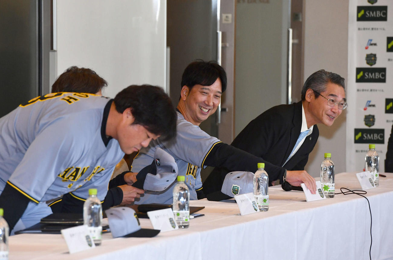 日本シリーズ前日の監督会議の会場に入り、笑顔で席につく阪神藤川監督（中央）。左端は安藤コーチ、右は嶌村球団本部長（撮影・岩下翔太）