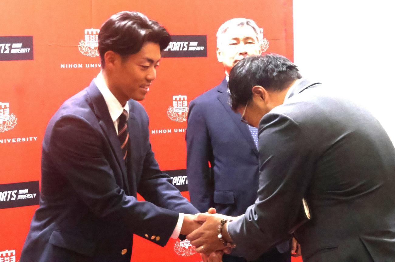 阪神東編成ディレクター（右）と握手するドラフト2位の日大・谷端（撮影・塚本光）