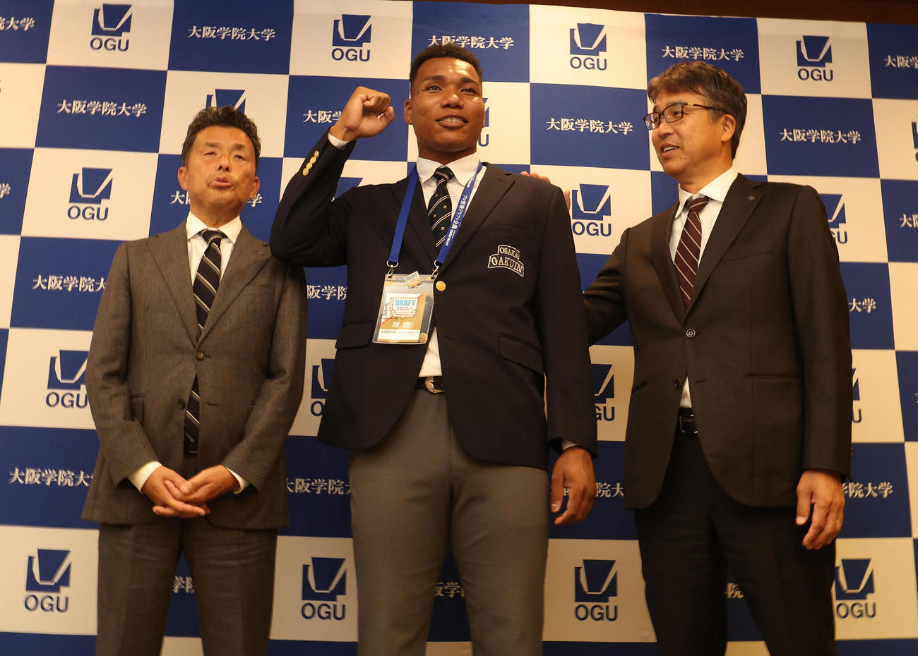 指名あいさつを終えて記念写真に納まる、左から日本ハム熊崎誠也スカウト、大阪学院大エドポロ　ケイン、大渕隆スカウト部長（撮影・白石智彦）