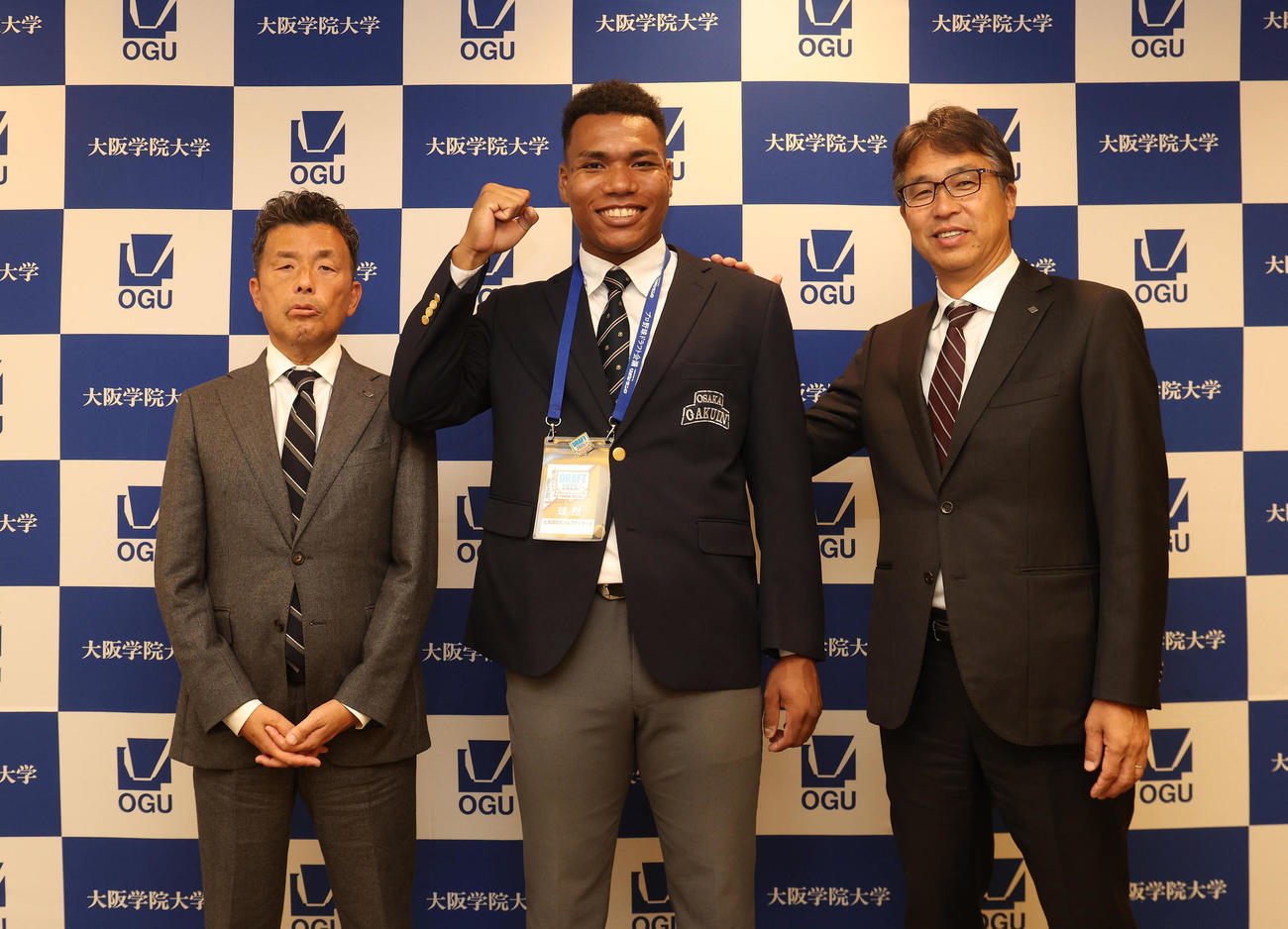 指名あいさつを終えて記念写真に納まる、左から日本ハム熊崎誠也スカウト、大阪学院大エドポロ　ケイン、大渕隆スカウト部長（撮影・白石智彦）