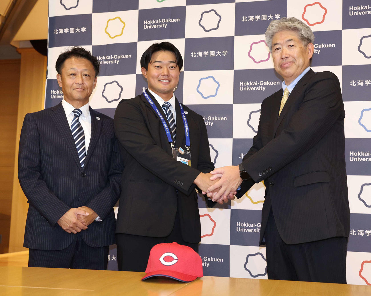 広島から4位指名された北海学園大の工藤（中央）は近藤スカウトから指名あいさつをうけ笑顔を見せる。左は島崎監督（撮影・黒川智章）
