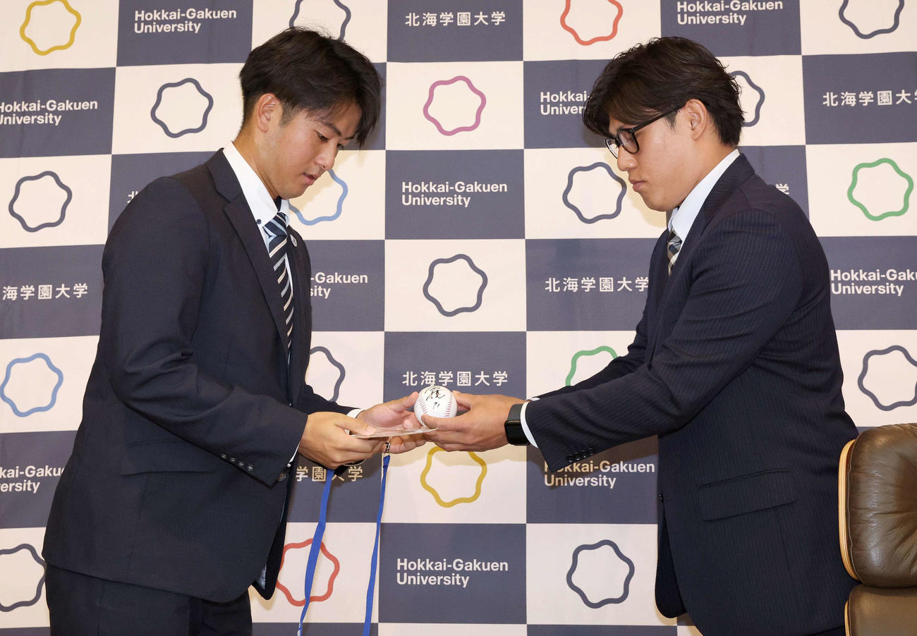 オリックスから5位指名された北海学園大の高谷（左）は岸田監督のサインボールを佐野アマチュアスカウトから手渡される（撮影・黒川智章）