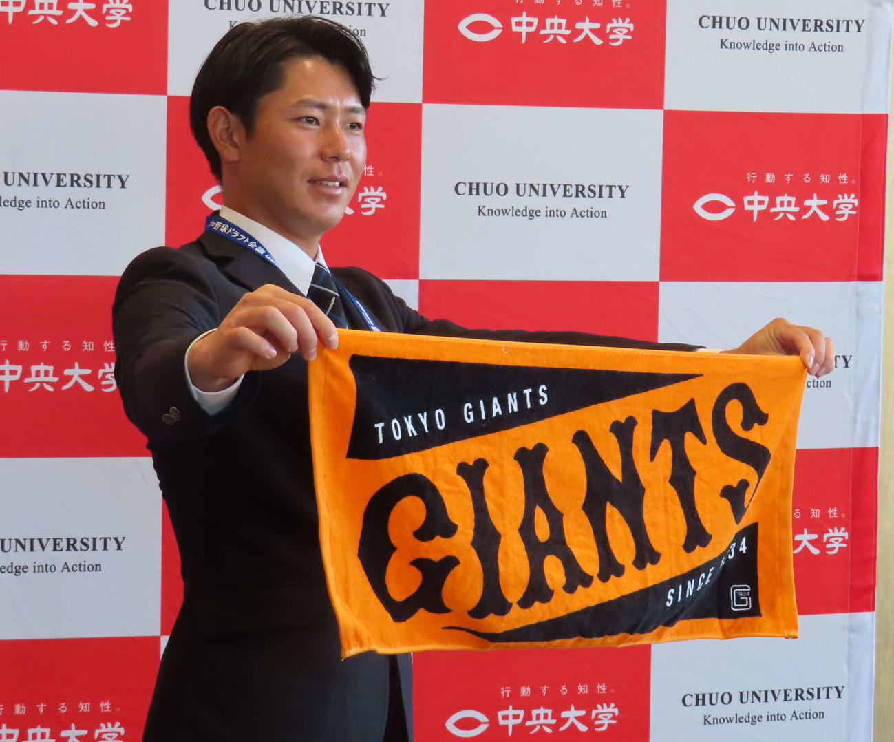 ジャイアンツのタオルを掲げ、笑顔を見せる巨人ドラフト4位の皆川（撮影・水谷京裕）