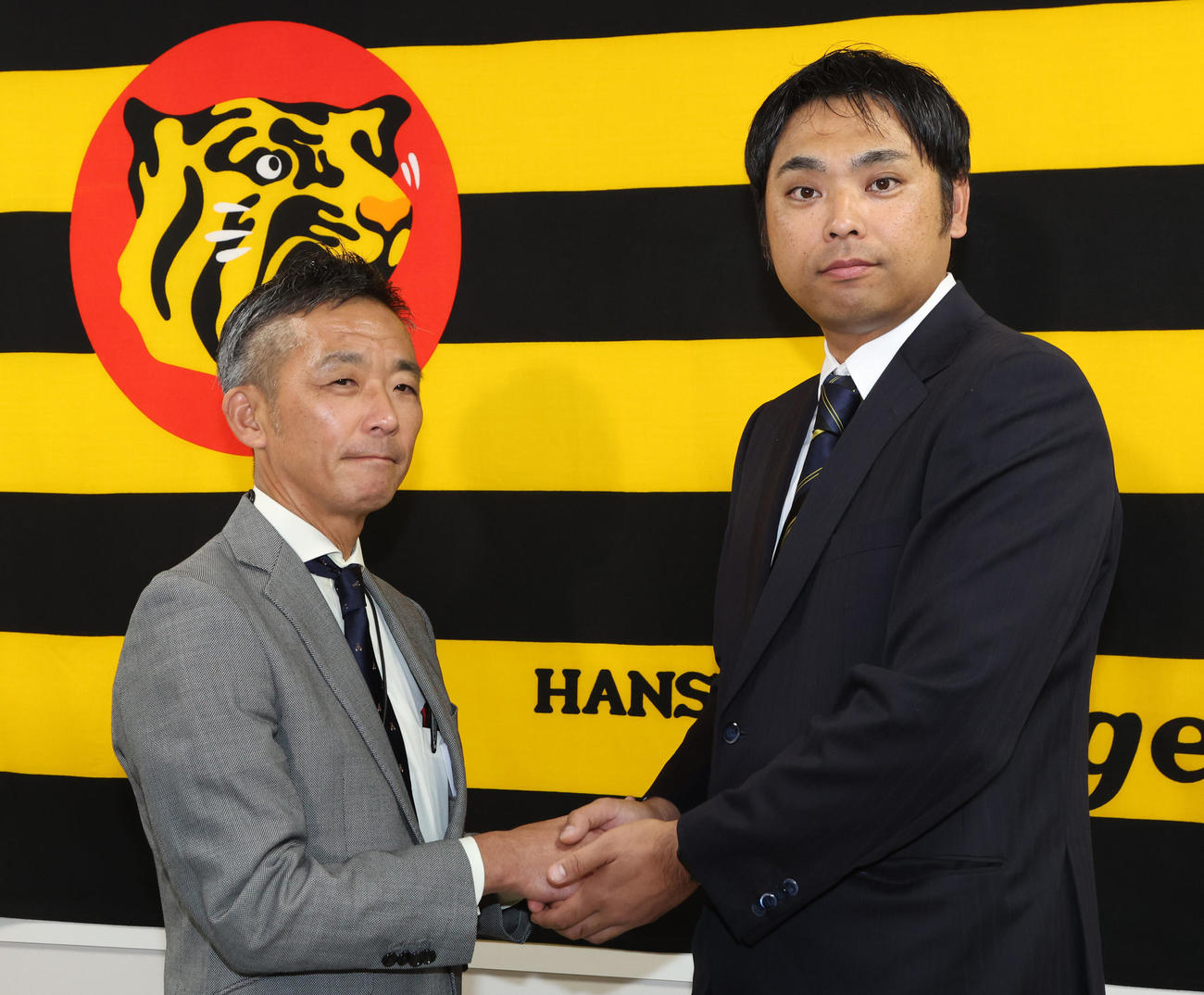 就任会見に臨んだ桑原新投手コーチ（右）は竹内球団副本部長と握手をかわす（撮影・西尾就之）