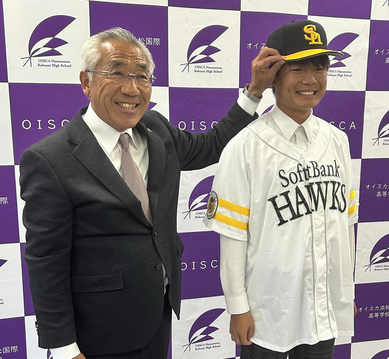 宮田担当スカウト（左）から帽子をかぶせてもらい、笑顔を見せるオイスカ浜松国際・大橋「令和」