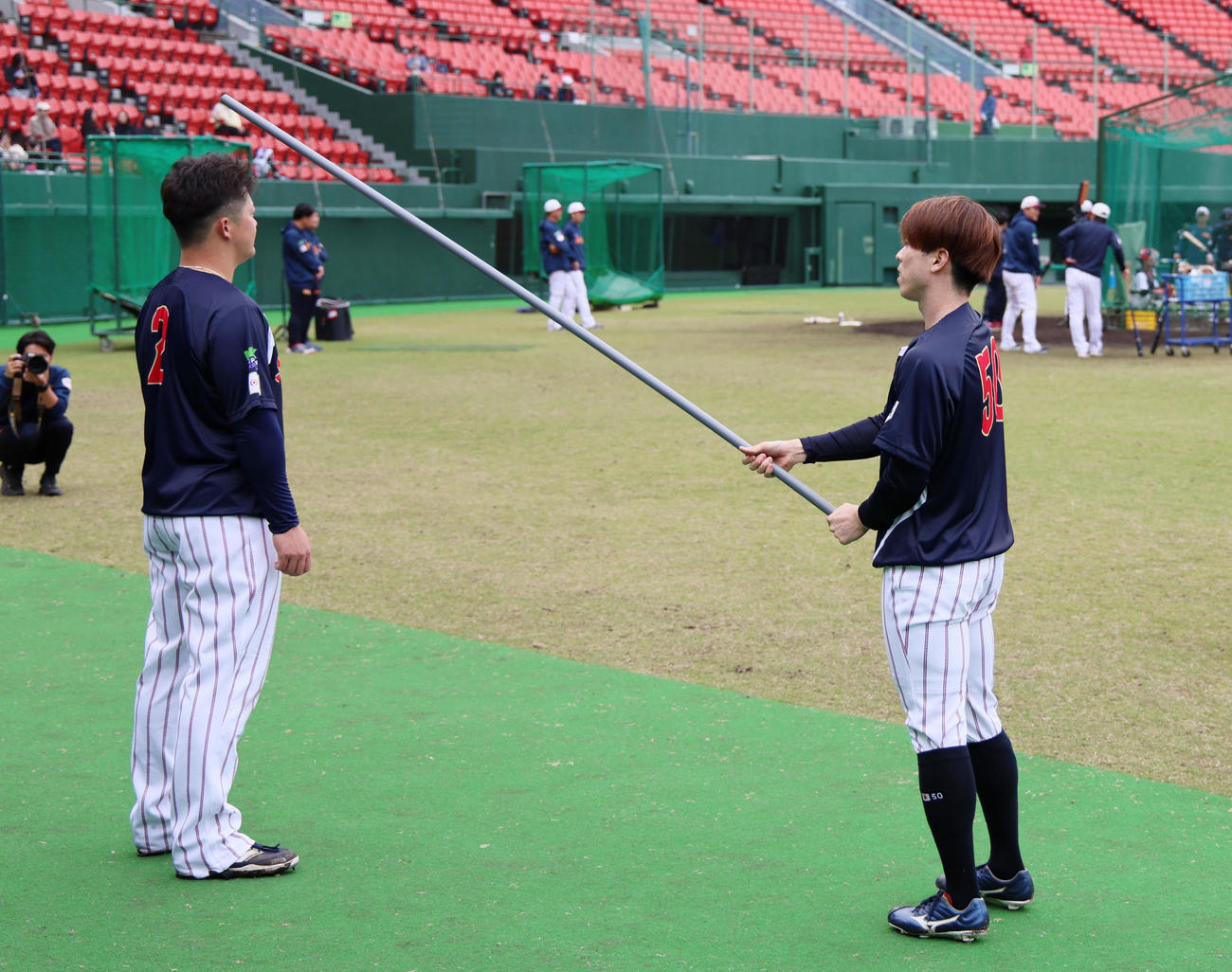 ベンチ前で細長い棒を使ってのトレーニングを行っていた五十幡（右）は、ちょっかいを出してきた牧の頭に棒をコツン（撮影・加藤哉）