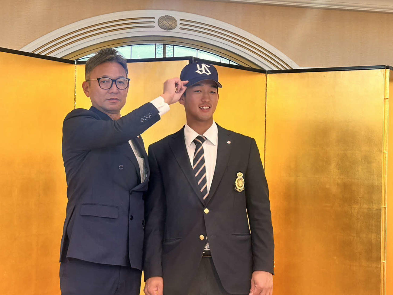 仮契約を終え、橿渕聡スカウトグループデスク（左）から帽子をかぶせてもらうヤクルト1位松下（撮影・平山連）
