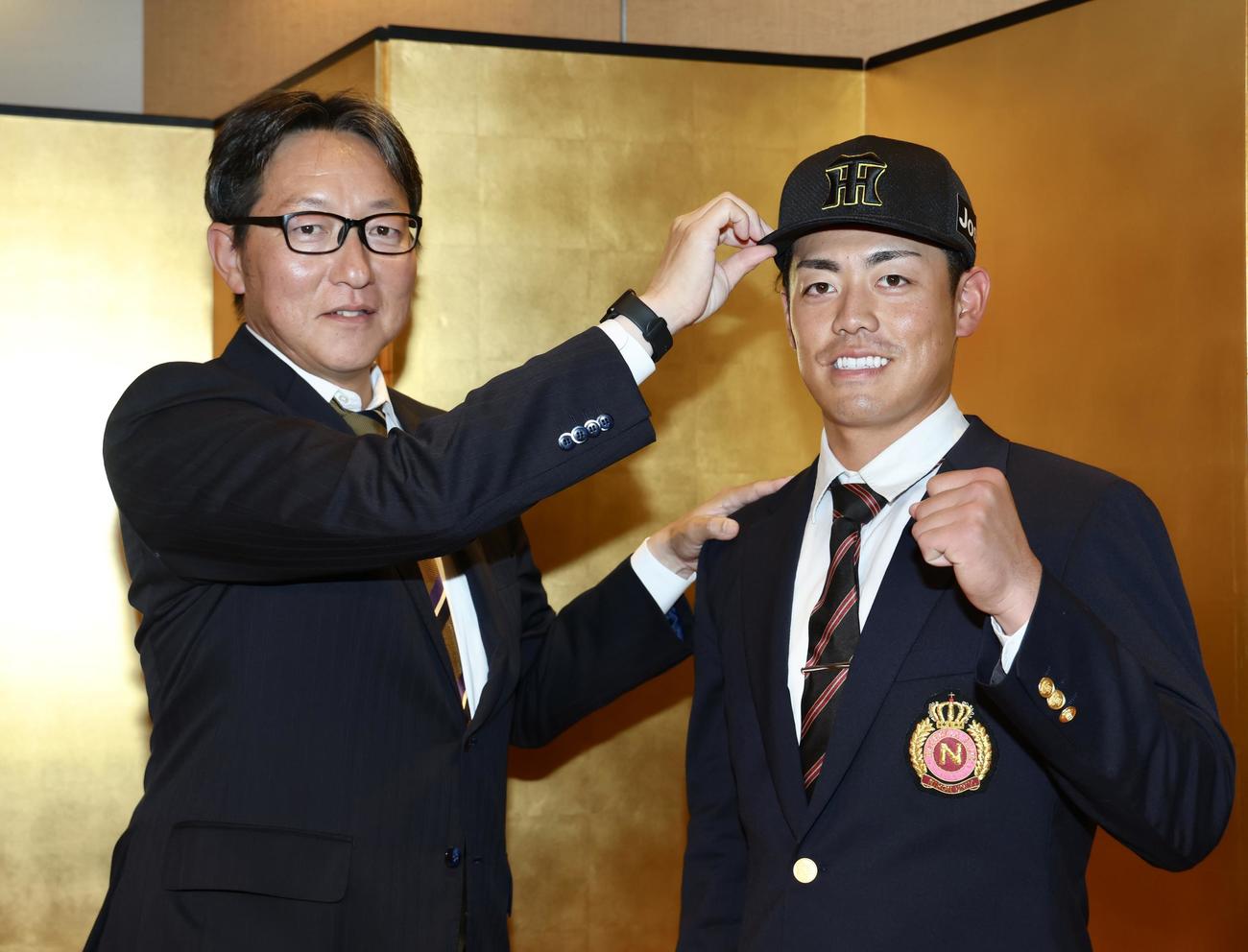 仮契約交渉を終え、吉野担当スカウト（左）に帽子を被らせてもらう阪神ドラフト2位の日大・谷端（撮影・河田真司）