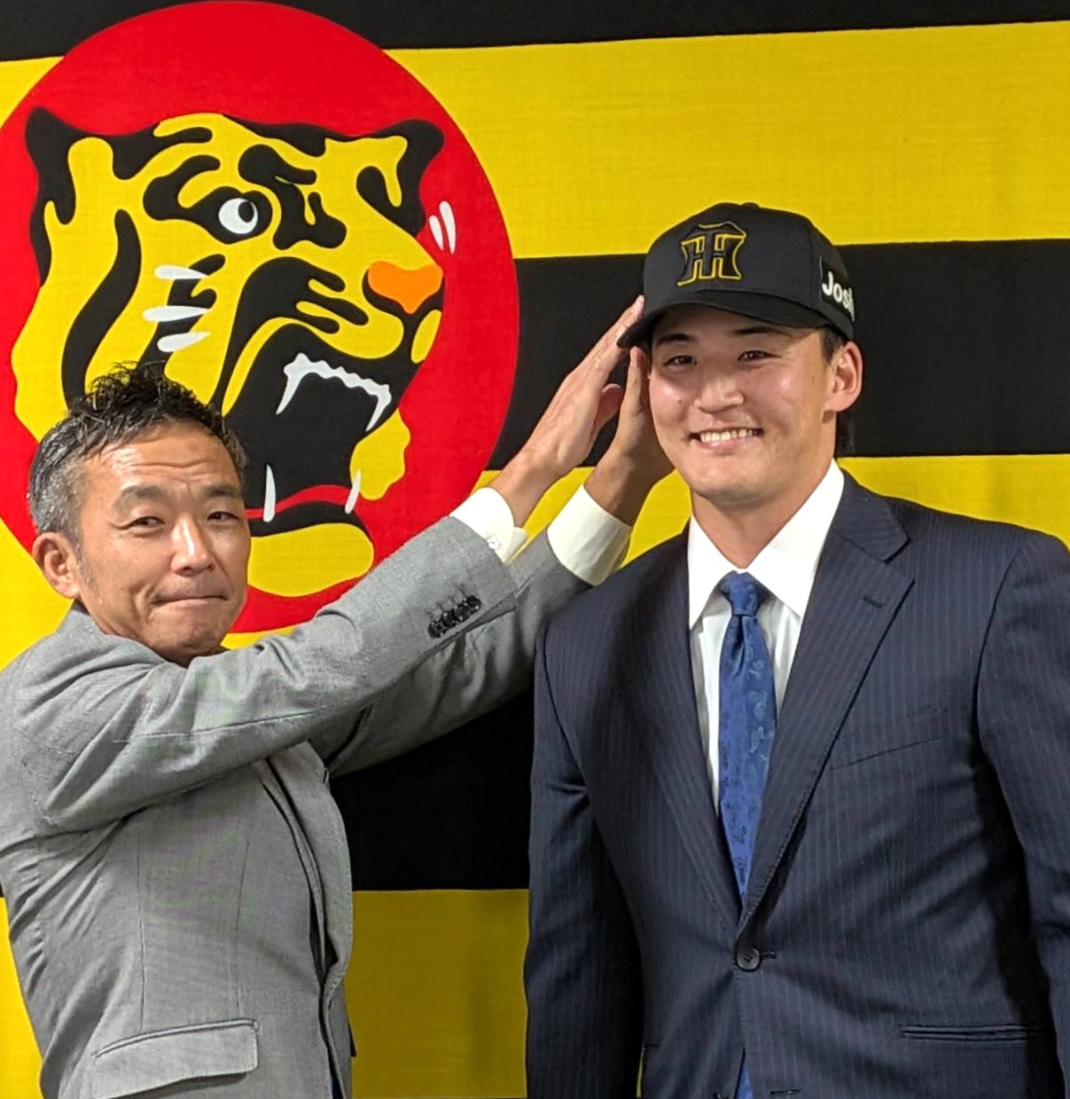 入団会見で竹内球団副本部長に帽子をかぶせてもらう阪神元山（撮影・柏原誠）