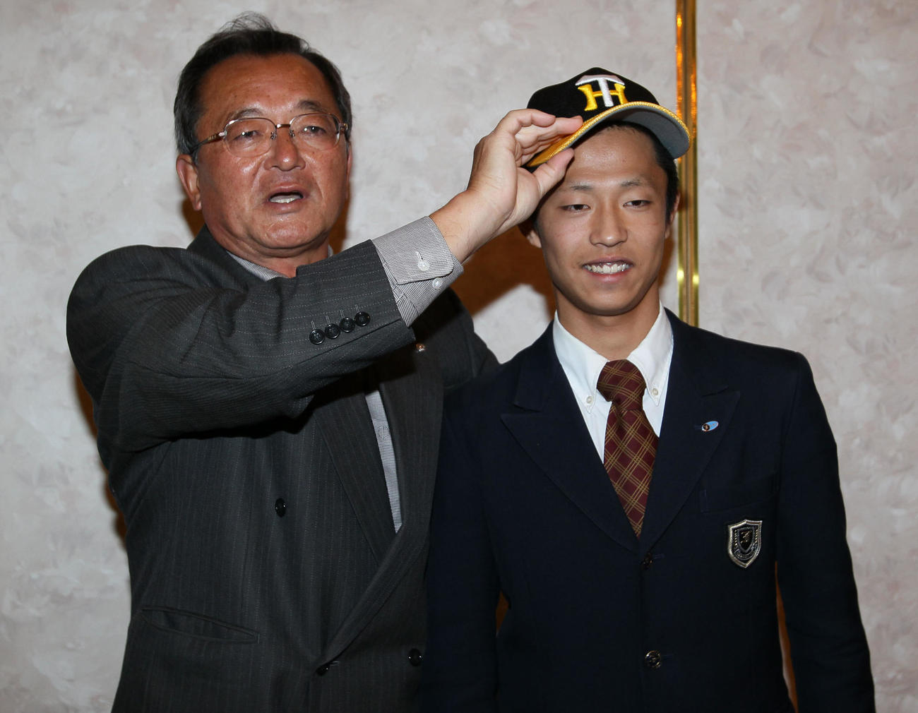 2010年11月、育成ドラフト2順目で指名された島本浩也（右）は仮契約をすませ池之上スカウトから帽子をかぶせてもらう
