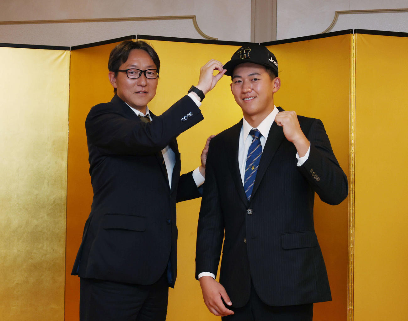仮契約を終え吉野スカウト（左）に帽子をかぶらせてもらう阪神ドラフト1位の創価大・立石（撮影・増田悦実）