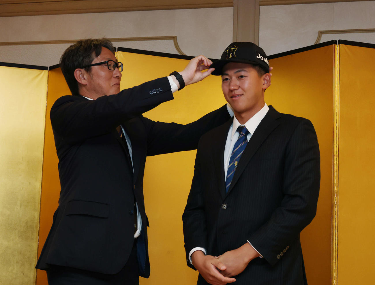 仮契約を終え吉野スカウト（左）に帽子をかぶせてもらう阪神ドラフト1位の創価大・立石（撮影・増田悦実）