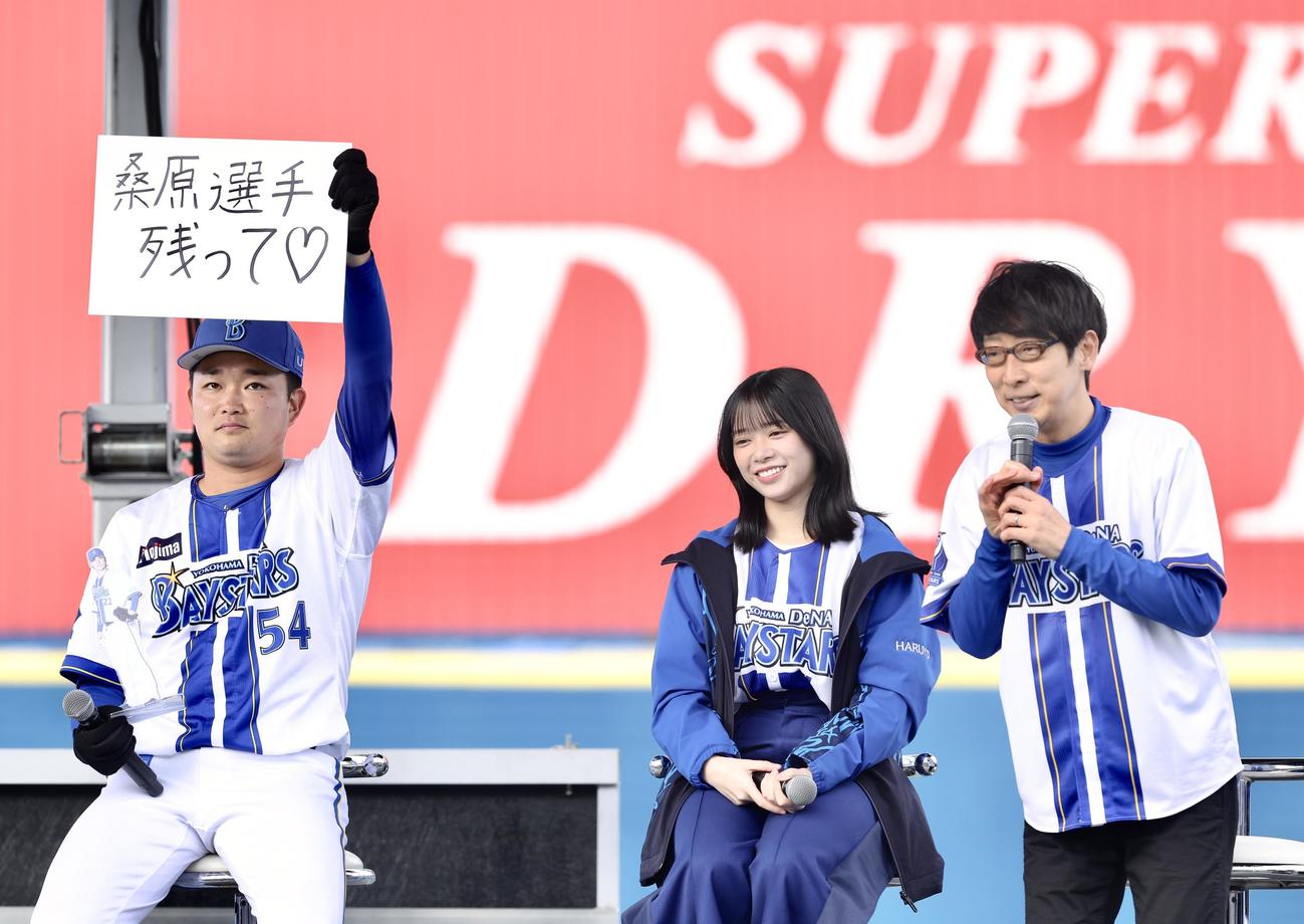 「桑原選手残って」と記されたフリップを掲げるDeNA石田裕（左）。右はダーリンハニー吉川正洋、中央は日向坂46山口陽世（撮影・河田真司）