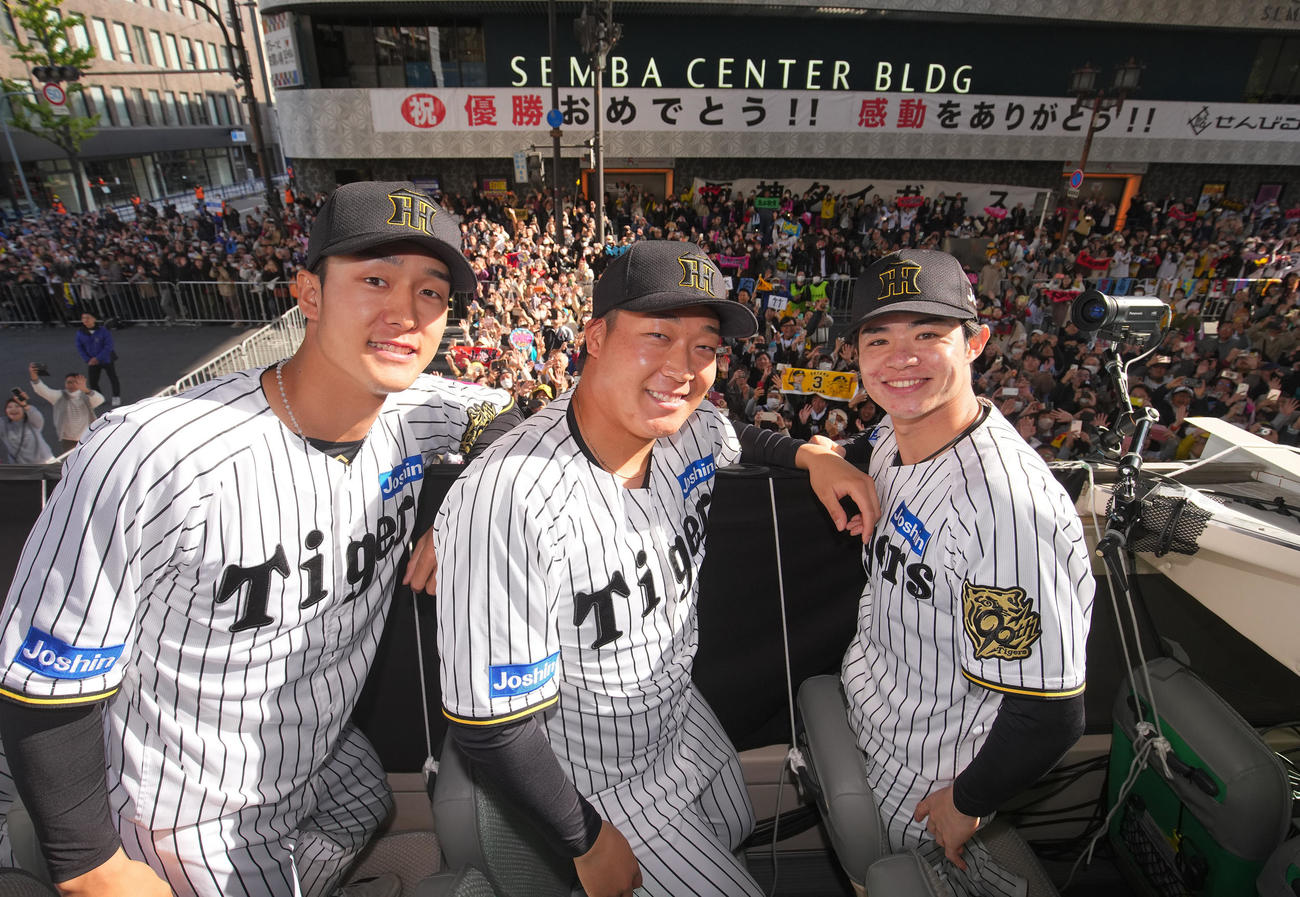 阪神優勝パレードで、船場センタービル前に集まった大勢のファンをバックに笑顔をみせる（左から）小幡竜平、大山悠輔、中野拓夢＝22日午前、大阪市中央区（代表撮影）