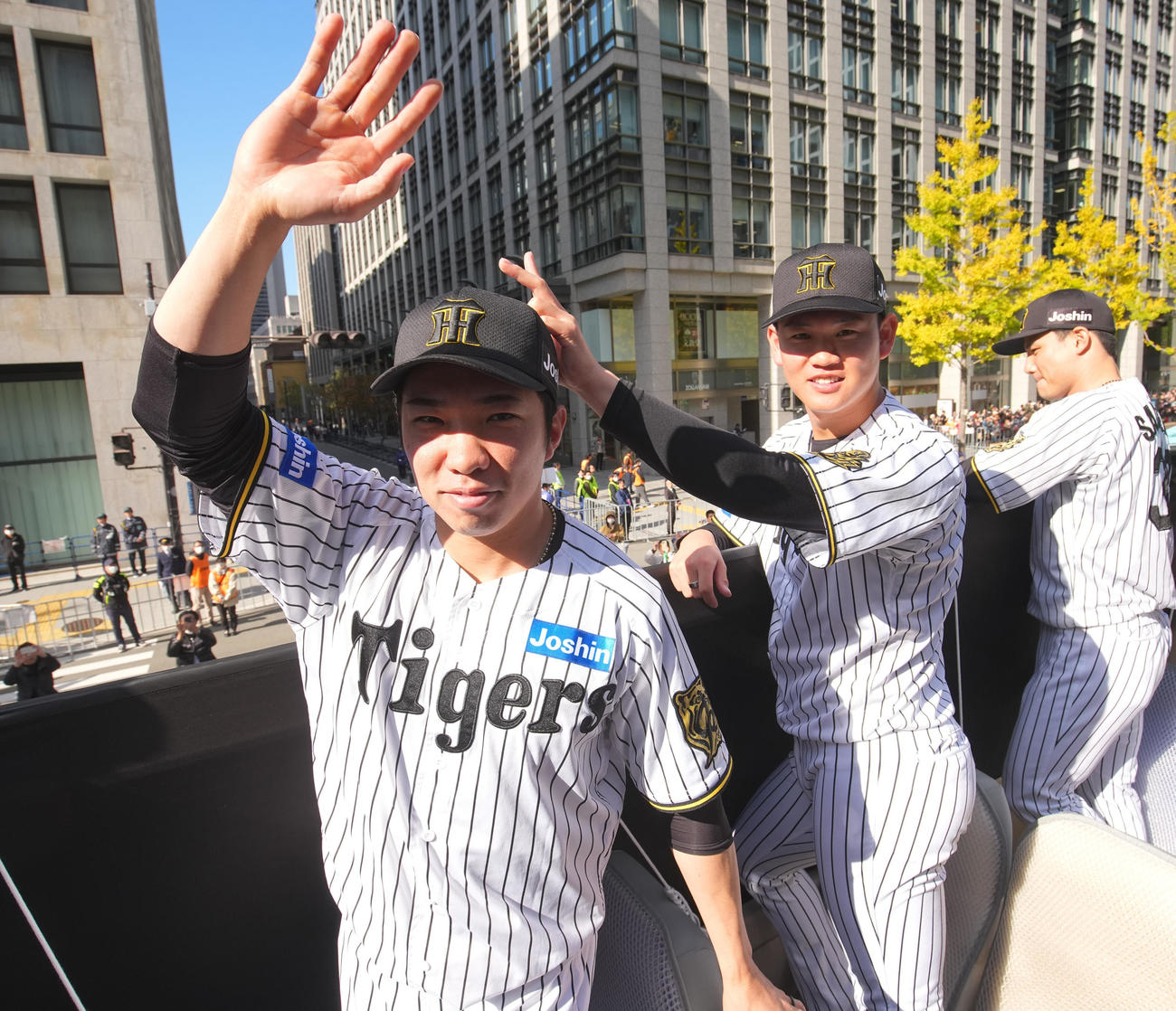 阪神優勝パレードでカメラに手を振る石井大智と及川雅貴（右）＝22日午前、大阪市中央区（代表撮影）