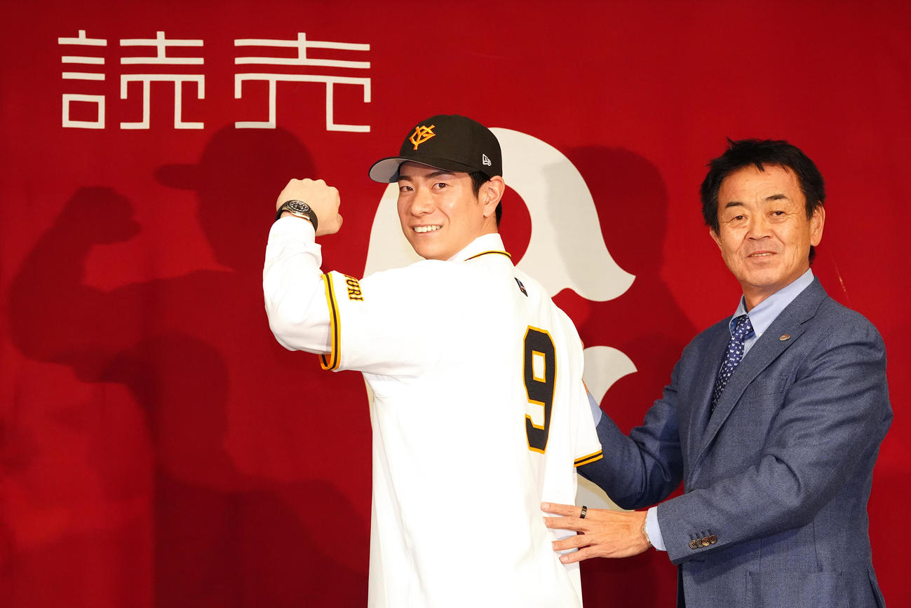 巨人入団会見に臨み、背番号「9」のユニホーム姿で写真に納まる松本（左）。右は水野編成本部長（撮影・江口和貴）