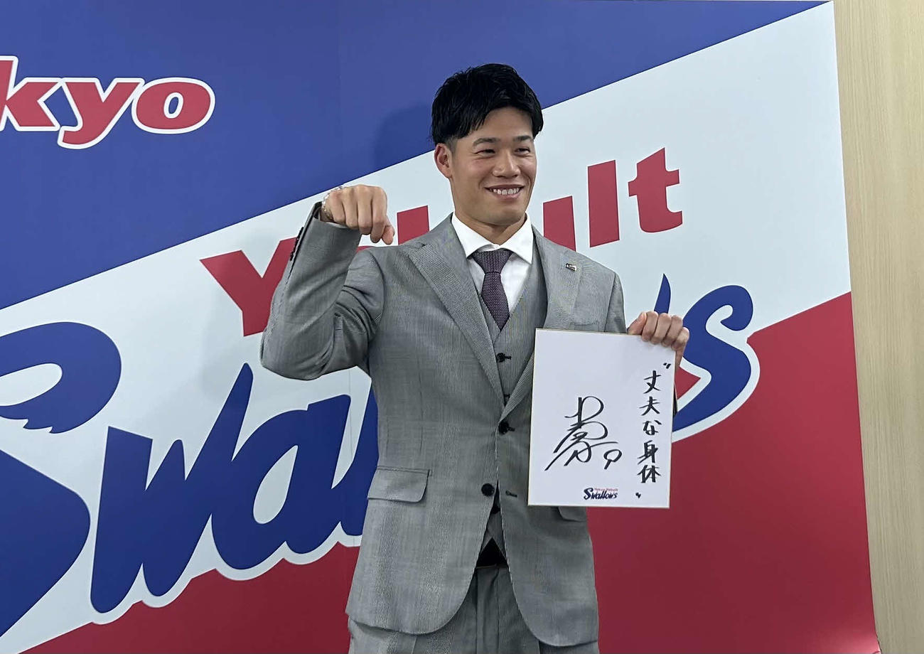都内の球団事務所で契約更改に臨み来季目標「“丈夫な体”」を記した色紙を掲げ、26年の干支である馬ポーズのリクエストに応えて写真に納まるヤクルト塩見
