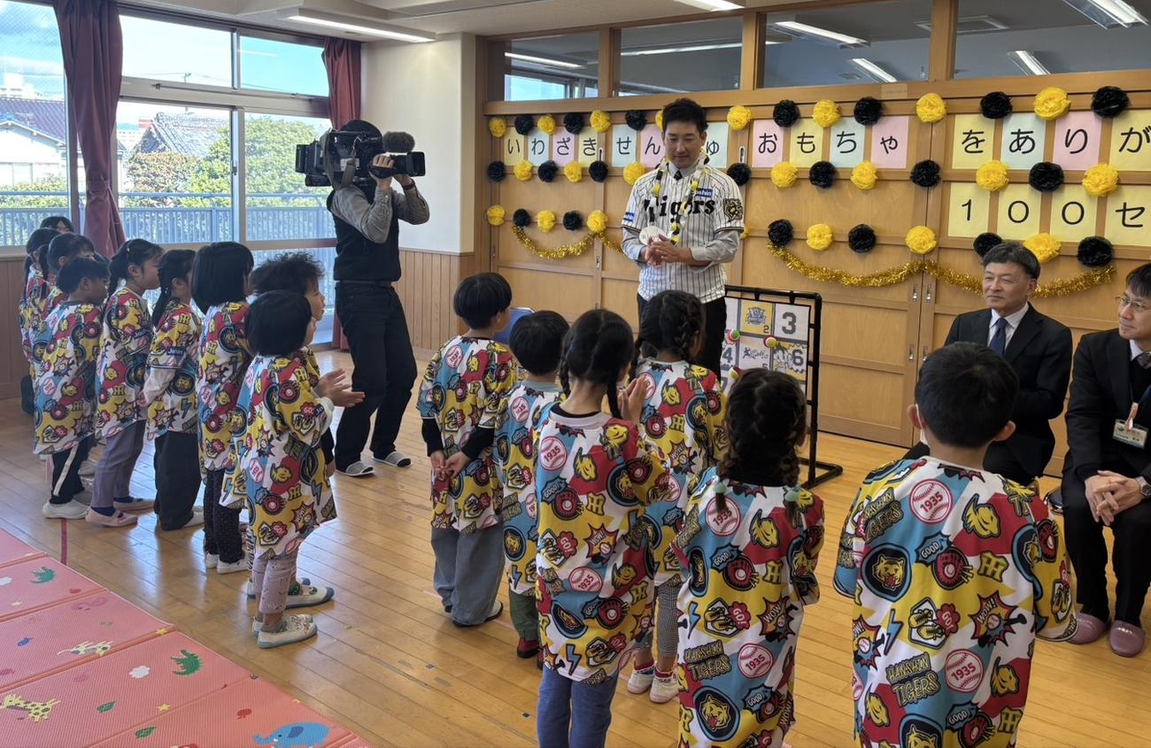 プレゼントされた「ありがとう」と書かれた紙製のメダルをかけて園児の前に立つ阪神岩崎（撮影・塚本光）