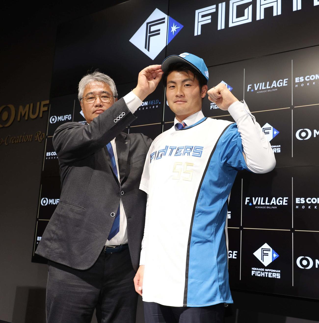 現役ドラフトで日本ハムに入団しユニホームに袖を通す菊地。左は木田GM代行（撮影・黒川智章）
