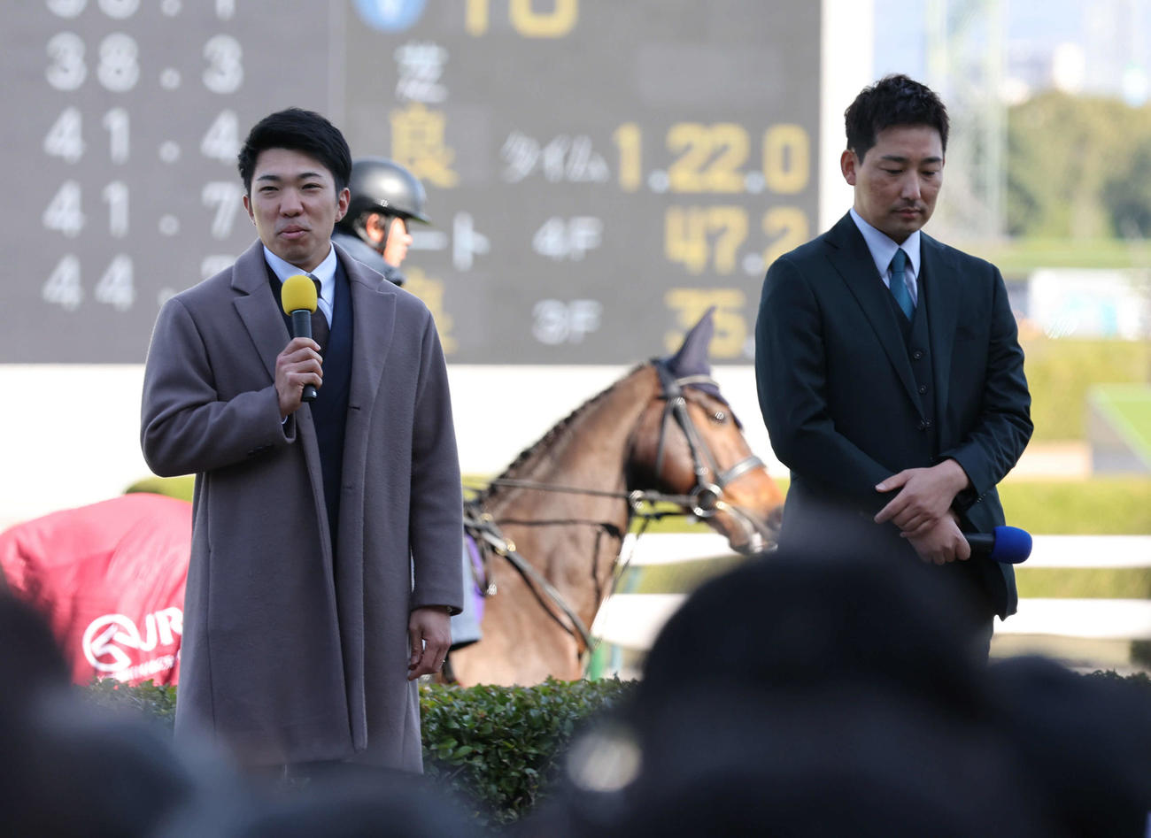 阪神競馬場で行われたトークショーに出演した阪神石井（左）と岩崎は後方を誘導馬が通る前、笑顔で話す（撮影・西尾就之）