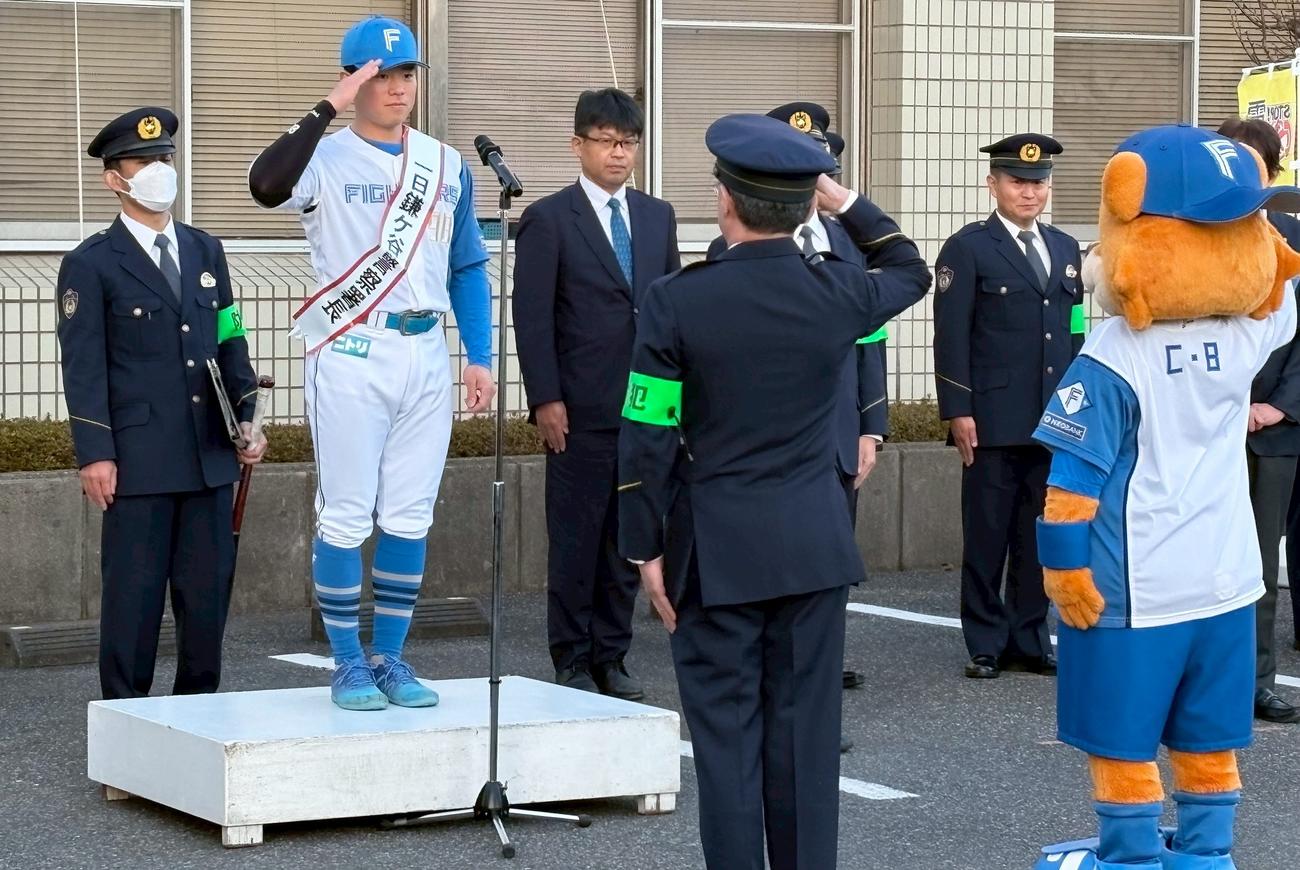 警察官とマスコットのカビーから報告を受け敬礼する日本ハム梅林（左から2人目）