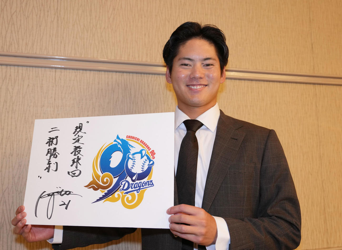 球団創立90周年記念ロゴパネルに来季の目標を掲げポーズを決める金丸夢斗