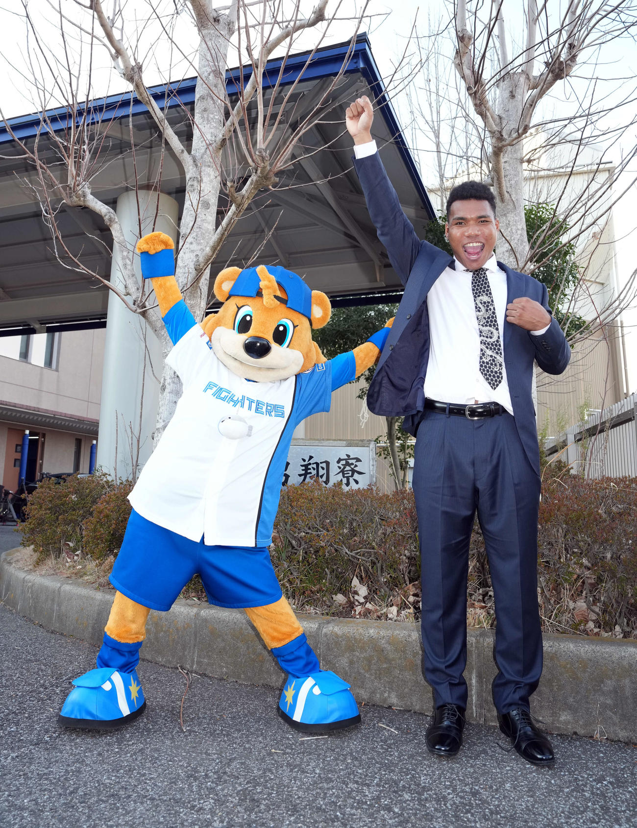 「勇翔寮」の前でポーズを決める日本ハムドラフト2位のエドポロ。左はマスコットのカビー（撮影・たえ見朱実）