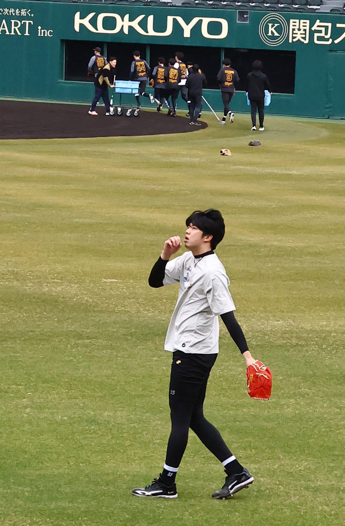 キャッチボールをする才木（手前）とノックを終えベンチに引き揚げる阪神新人の選手たち（撮影・上田博志）