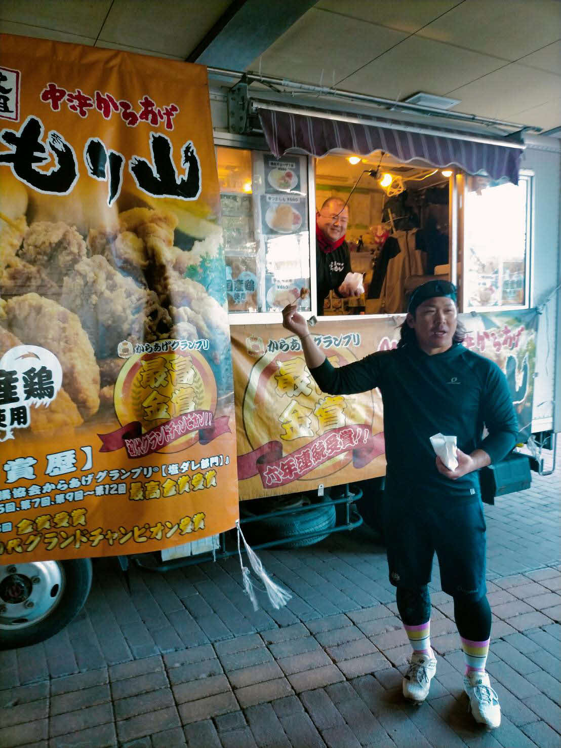 甲斐は昼食で振る舞った中津からあげ店の前でポーズ