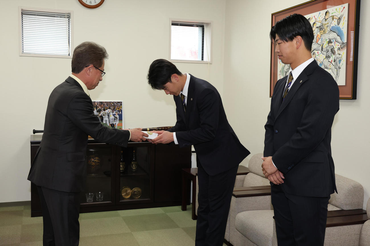 阪神の20歳記念品贈呈式で粟井一夫社長（左）から記念品を受け取る山田（中央）。右は百崎