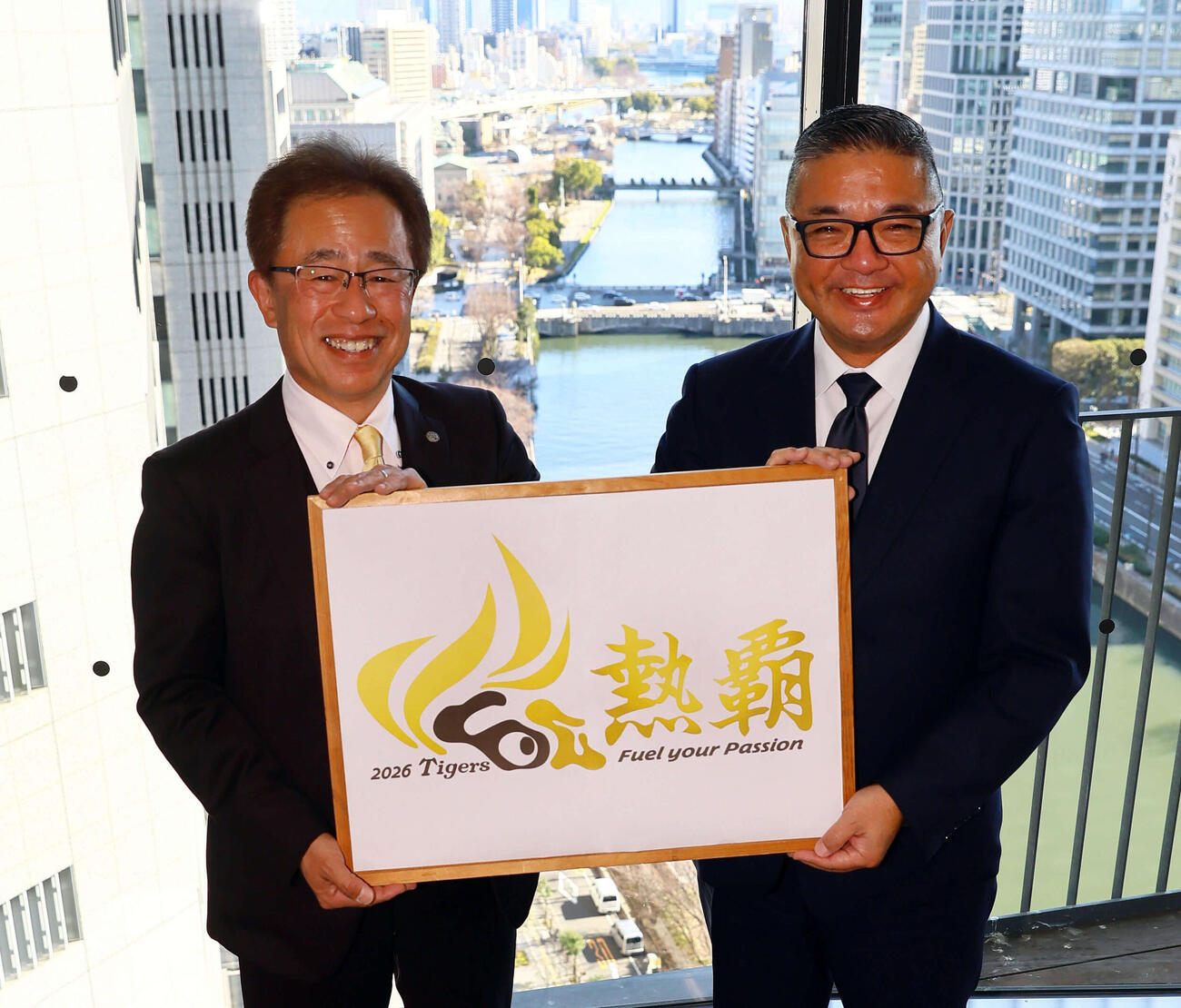 新年のあいさつに日刊スポーツ西日本本社を訪れた阪神粟井球団社長（左）は、日刊スポーツ新聞西日本中山代表取締役社長とチームスローガンの「熱覇」を手に笑顔を見せる（2026年1月6日撮影）