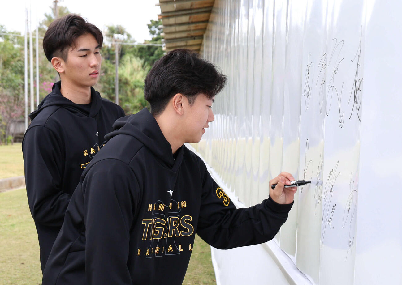 宜野座に新しくできた「めんそー路」の壁にサインする門別。左は今朝丸（撮影・西尾就之）