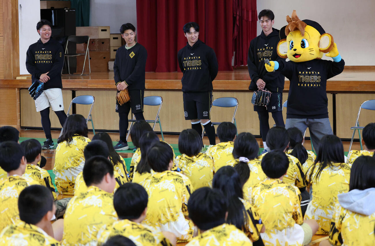沖縄・うるま市の田場小学校を訪問し、生徒の前で話す（左から）阪神森下、谷端、井坪、今朝丸。右はマスコットのキー太（撮影・西尾就之）