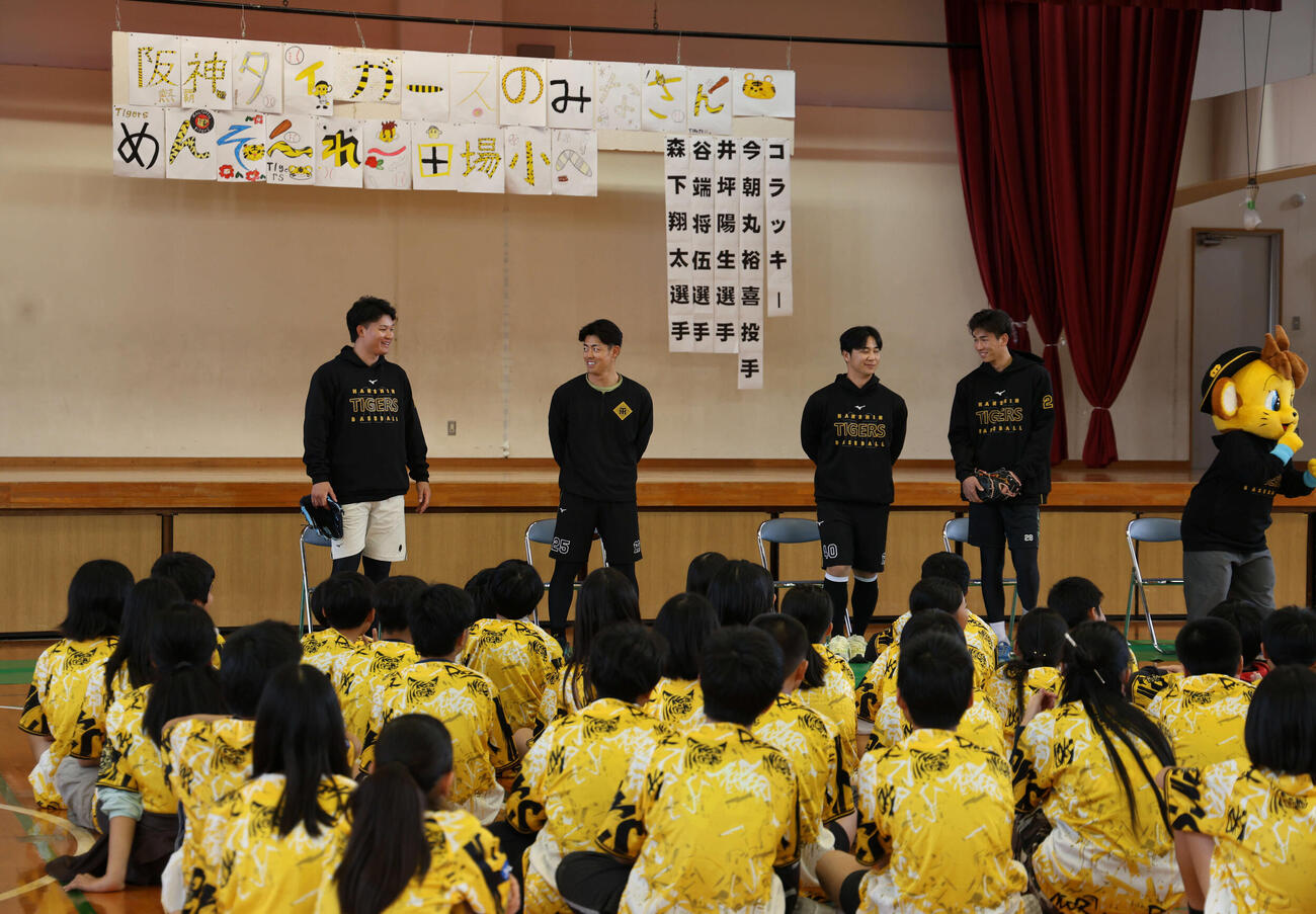 沖縄・うるま市の田場小学校を訪問し、生徒の前で話す（左から）阪神森下、谷端、井坪、今朝丸。右はマスコットのキー太（撮影・西尾就之）