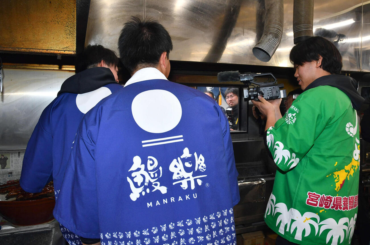 キャンプ休日、焼いたうなぎにタレをかける高橋（左）をカメラで撮影するソフトバンク稲川（撮影・岩下翔太）