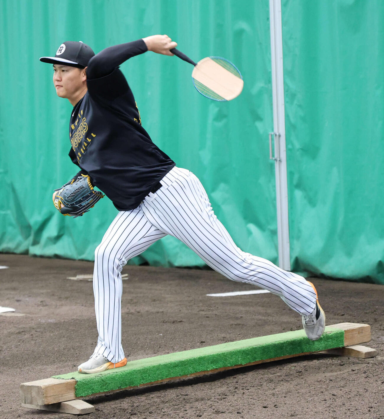 ブルペンで平均台の上でバドミントンのラケットを振る練習をする阪神及川（撮影・西尾就之）