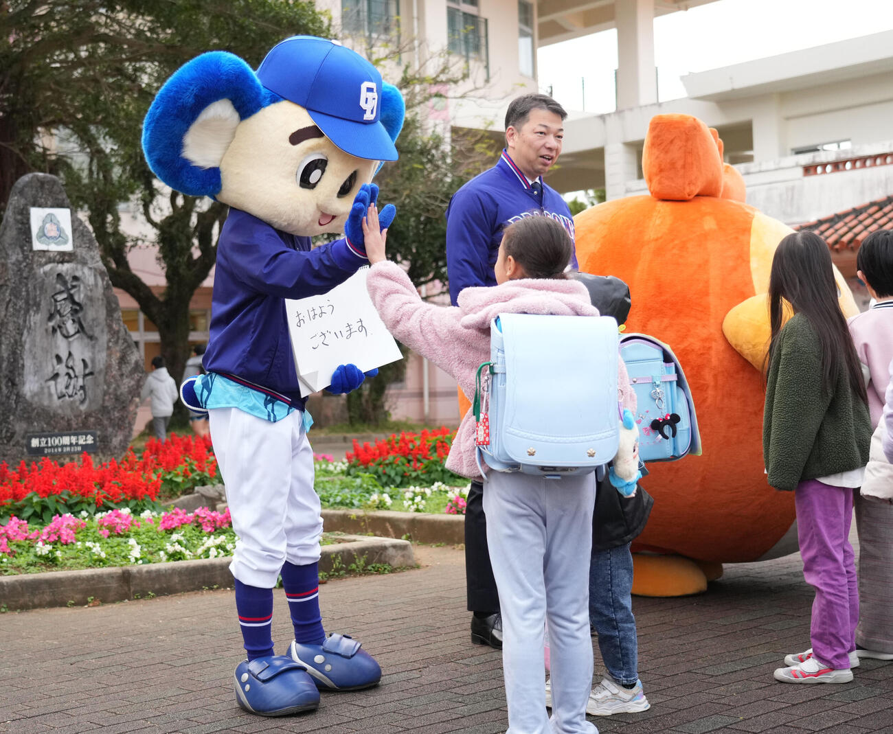 キャンプ地の小学校を訪れあいさつ運動を行う奥・左からドアラ、北谷町の渡久地町長、ちーたん（撮影・森本幸一）