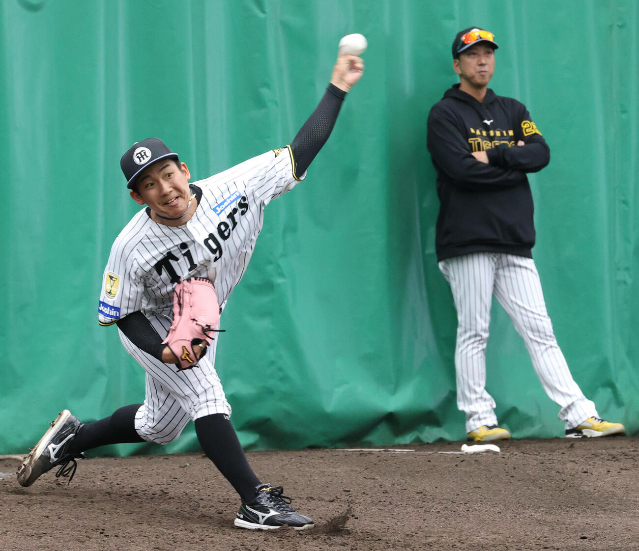 ブルペンで阪神藤川監督（右）が見守る中、投球する伊原（撮影・上山淳一）