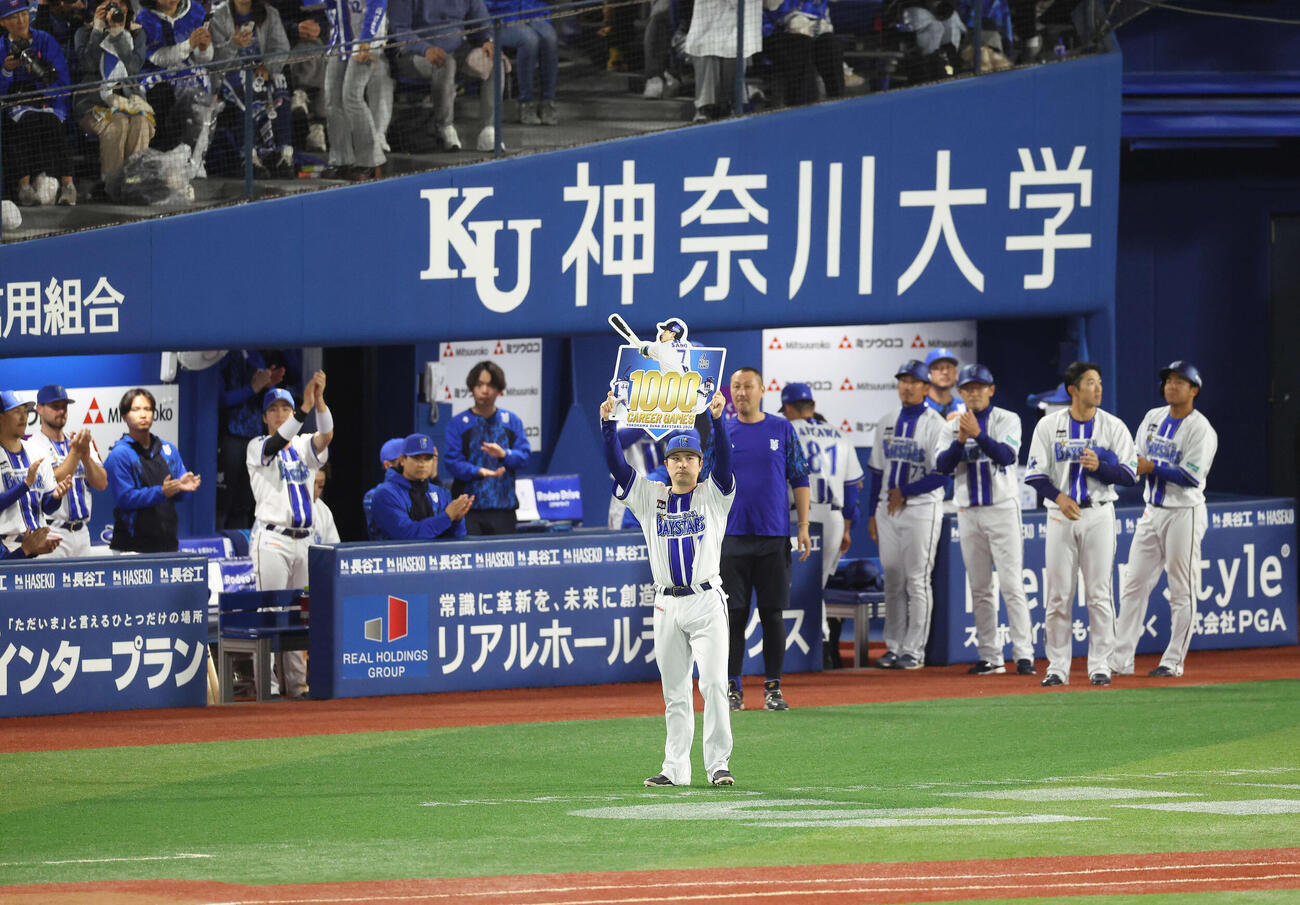 DeNA対阪神　1000試合出場を果たし、記念ボードを手に観客の声援に応える佐野恵太（中央）＝2026年4月22日　