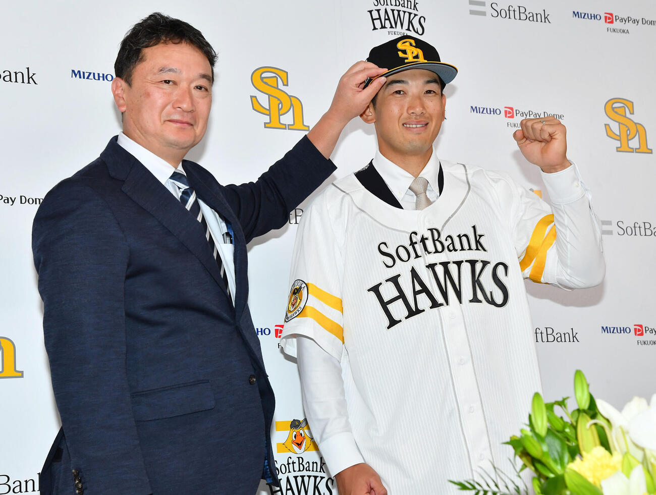入団会見で三笠杉彦取締役GM（左）から帽子をかぶせてもらい、ガッツポーズするソフトバンク山本祐大（撮影・岩下翔太）