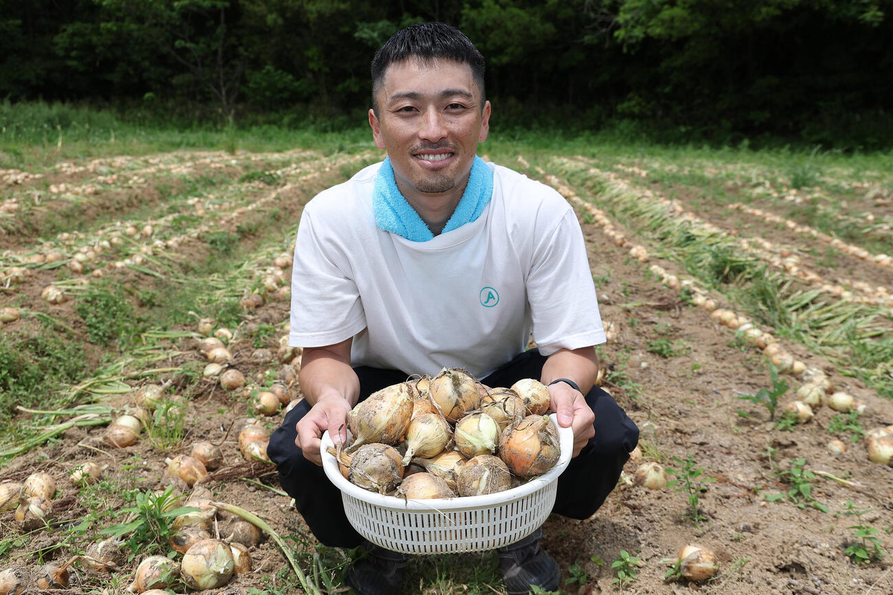 「元オリックス福田周平さんと！新玉ねぎ収穫＆”周平ファーム”お手伝い体験」　収穫した新玉ねぎを手に笑顔の元オリックスの福田周平氏（撮影・前田充）＝2026年5月24日