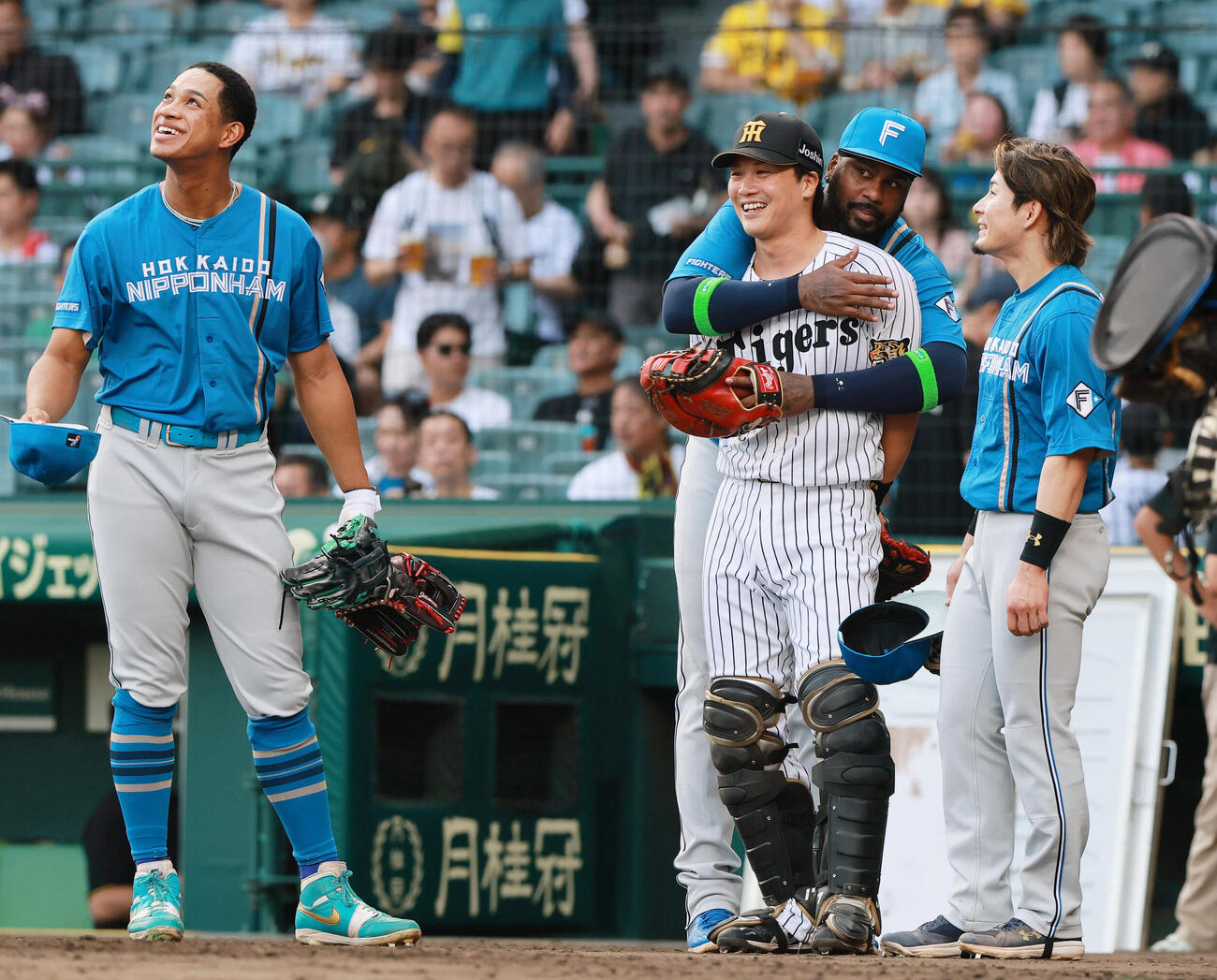 セ・パ交流戦　阪神対日本ハム1回戦　阪神対日本ハム　試合前、阪神伏見寅威（左から2人目）に抱きつく日本ハムフランミル・レイエス。左は日本ハム万波中正、右は日本ハム水野達稀（撮影・上山淳一）＝2026年5月26日..