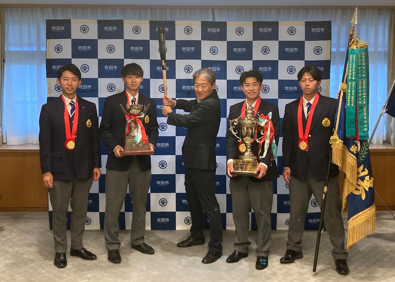 吹田市役所に日本一の報告に訪れた関大野球部メンバー。右から中原海晴副主将、森内大奈主将、バットを構える後藤圭二市長、米沢友翔副主将、大田侑季主務