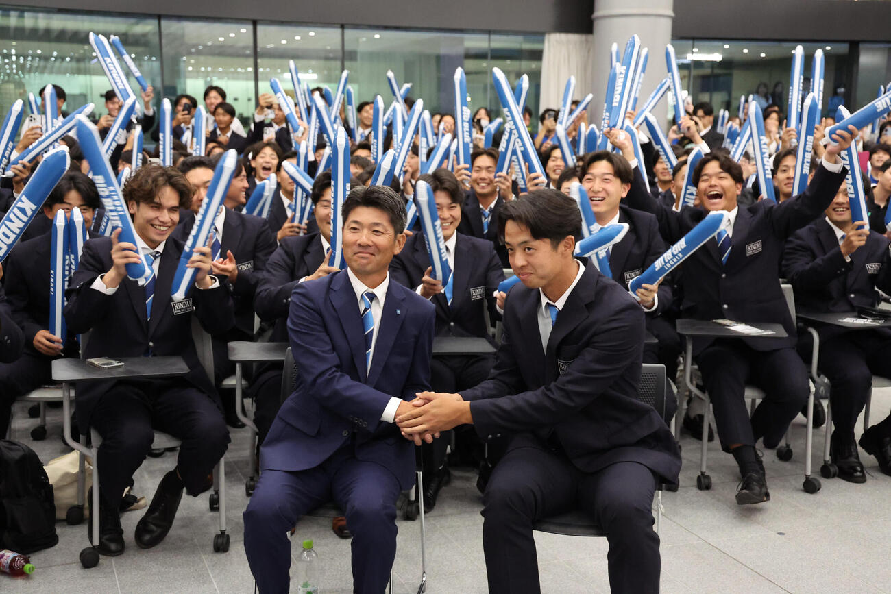競合の末、中日1位が決まった近大・宮原廉（右）は中継を見ながら松丸文政監督と握手をかわす（撮影・西尾就之）