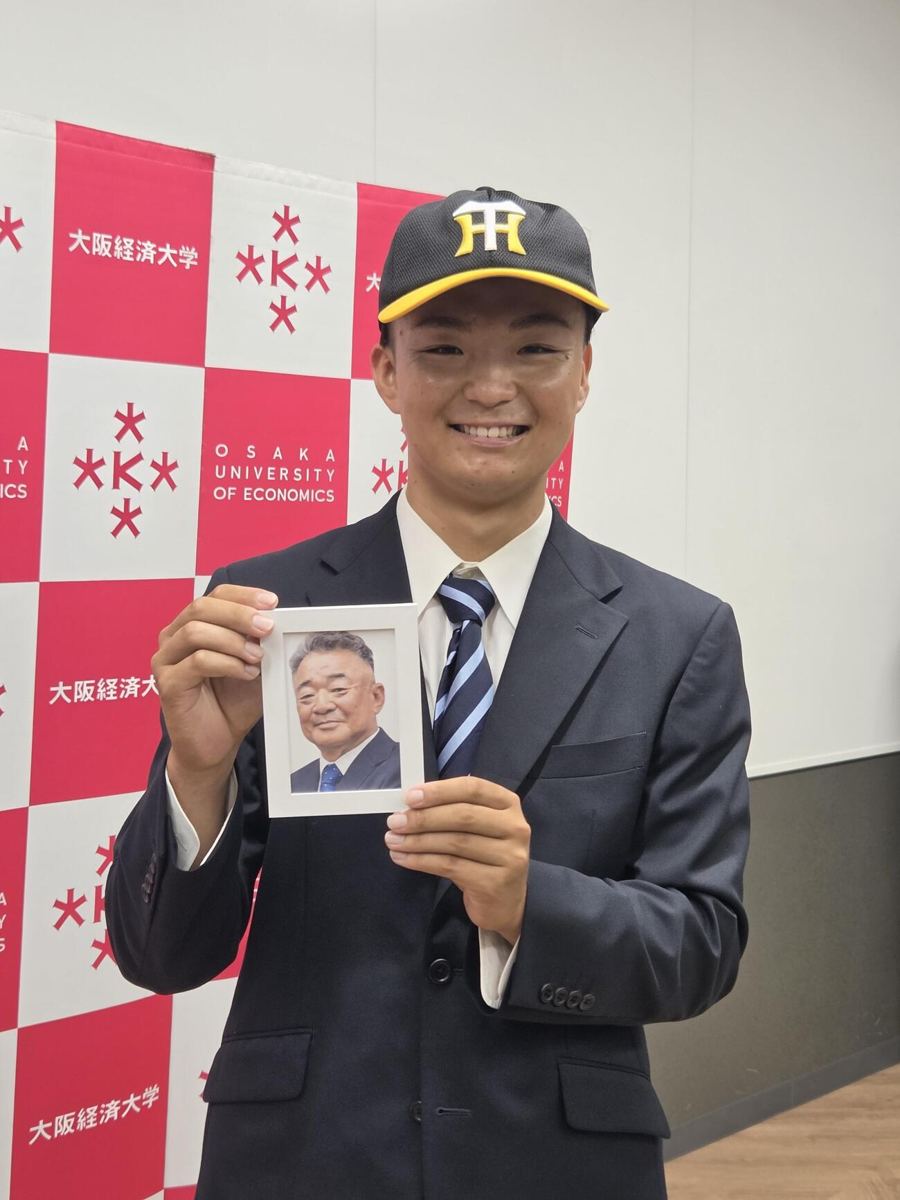 阪神3位指名の大経大・常深颯大投手は他界した前監督の故・高代延博さんの遺影とともに記者の囲みに応じた（撮影・寺尾博和）