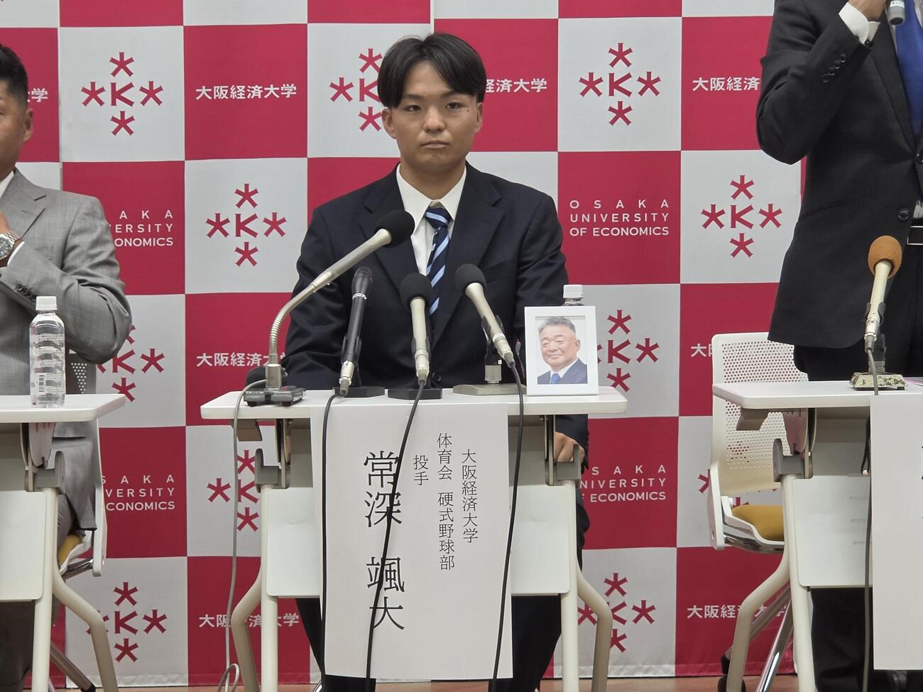 前監督の故・高代延博氏の遺影をとともに記者会見する大経大・常深颯太投手（撮影・寺尾博和）