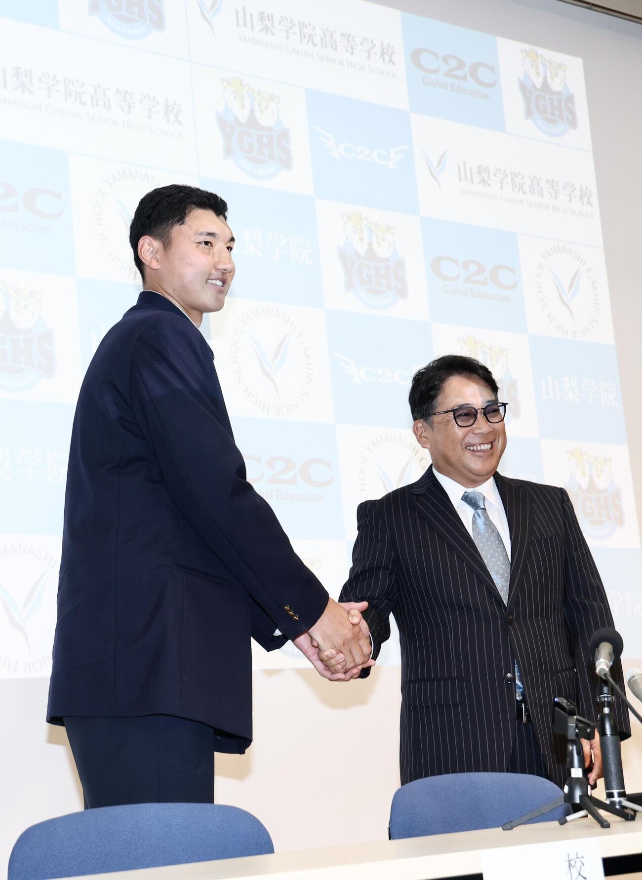 日本ハムから1位指名を受けた山梨学院・菰田陽生（左）は吉田洸二監督と握手を交わす（撮影・河田真司）