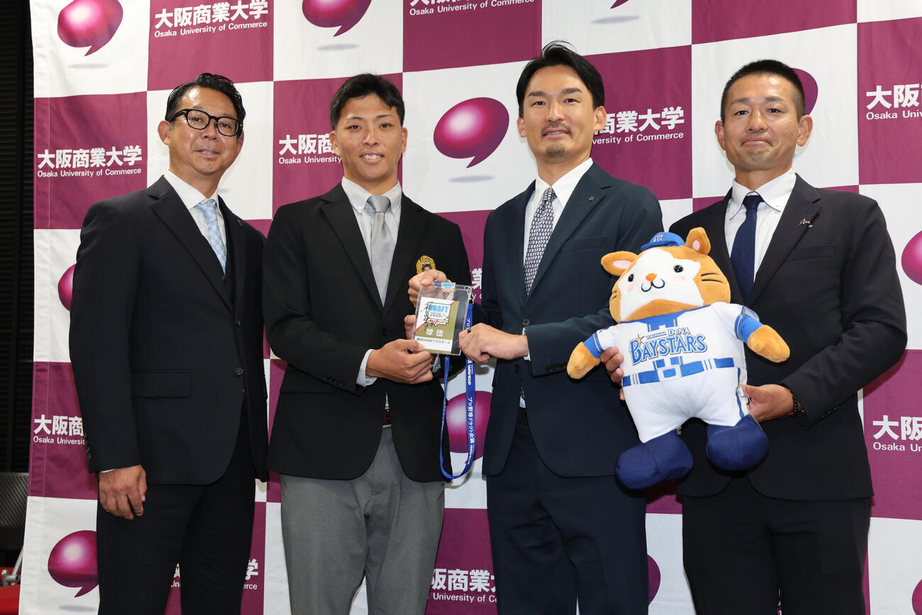 DeNA1位の大商大・星野世那（左から2人目）は（左から）八馬幹典アマスカウティンググループリーダー、1人おいて長谷川竜也編成部長、藤田和男スカウトから指名あいさつを受け、相川亮二監督のサイン入りパスを手に写真に納まる（撮影・西尾就之）