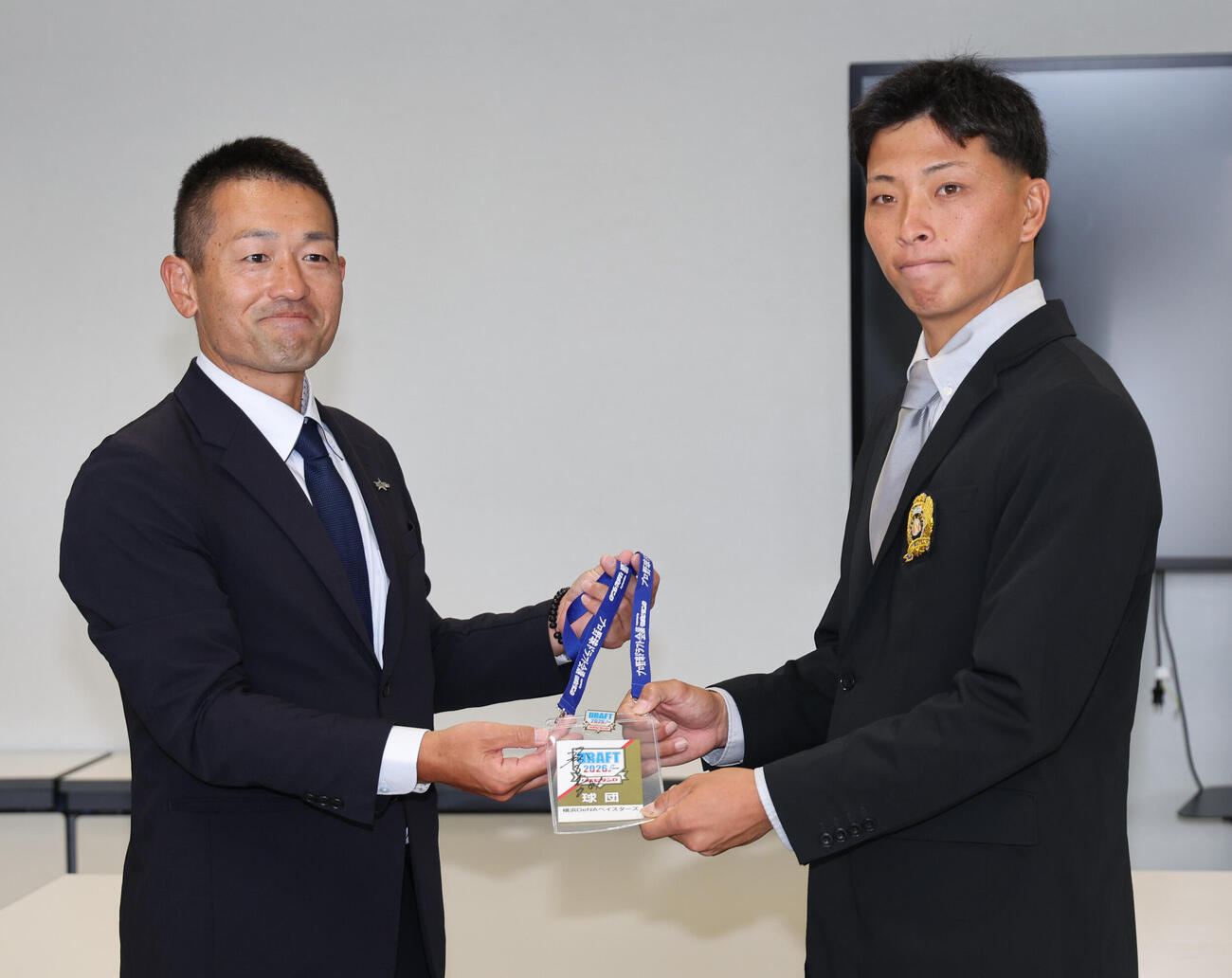 DeNA1位の大商大・星野世那（右）は相川亮二監督のサイン入りパスを藤田和男スカウトから受け取る（撮影・西尾就之）